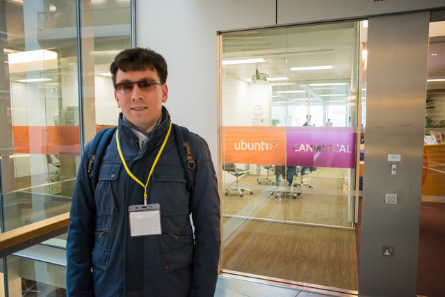 Молодой человек стоит рядом с эмблемой компании Canonical около входа в её офис